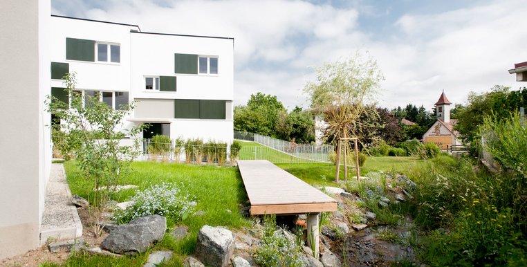 Das Bild zeigt den Garten eines Reihenhauses in Neustift Innermanzing, mit einem kleinen Steg und grünen Büschen.
