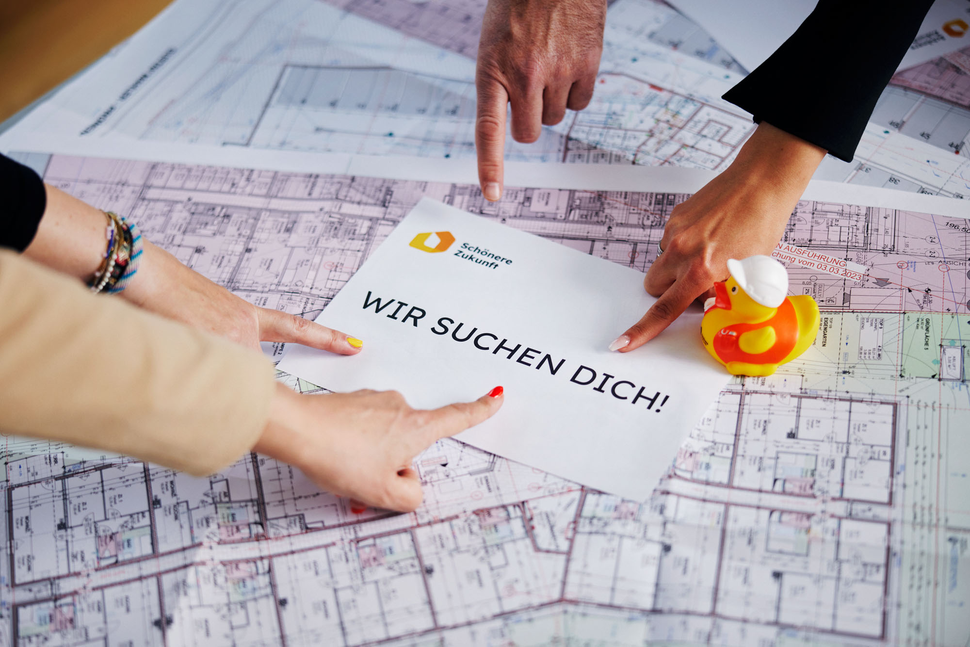 Hände zeigen auf ein Blatt Papier mit der Aufschrift "Wir suchen Dich"