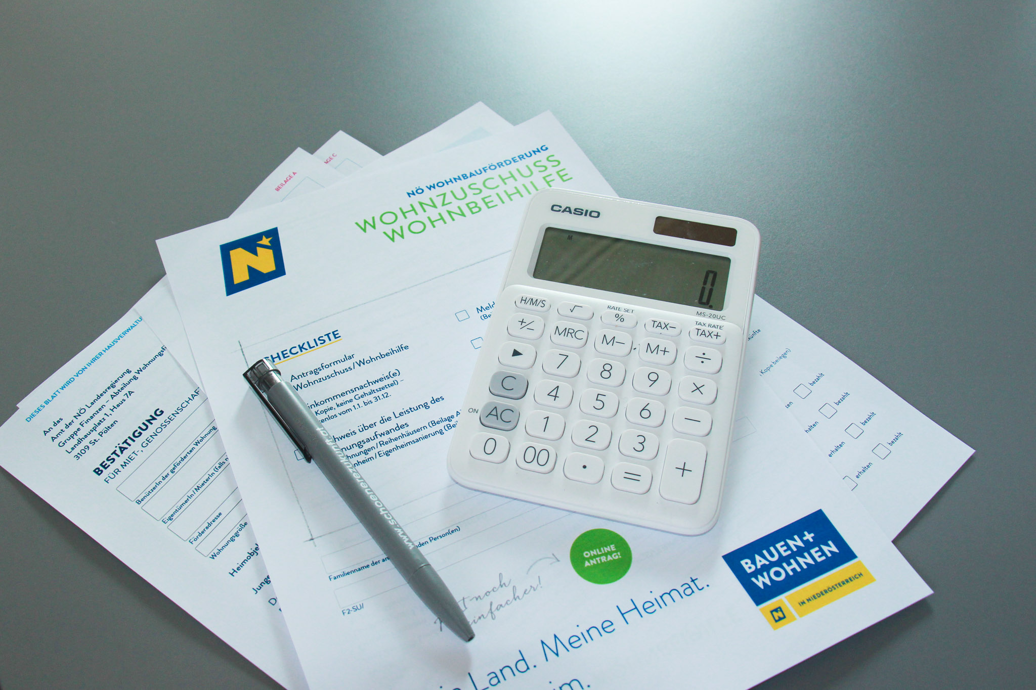 Das Bild zeigt eine Antrag auf Wohnzuschuss, einen Taschenrechner und einen Kugelschreiber.